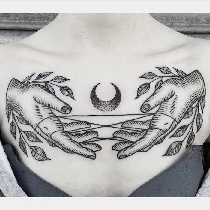 chest tattoos for women, crescent moon, hands pulling stings, grey bra and sweater