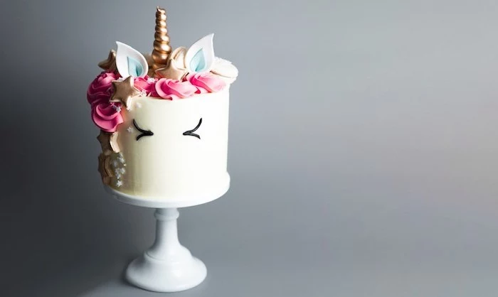 white cake stand, grey background, unicorn cake, white frosting covered with pink roses and sprinkles