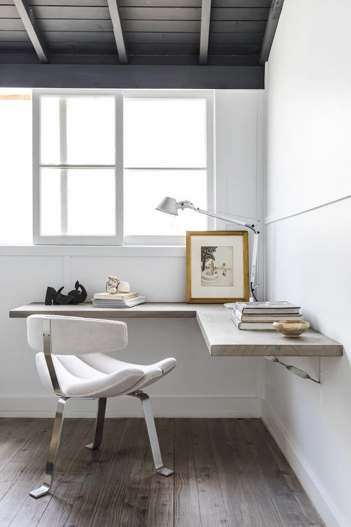 white walls, white velvet chair, office pictures, wooden desk with a desk lamp and books, wooden ceiling