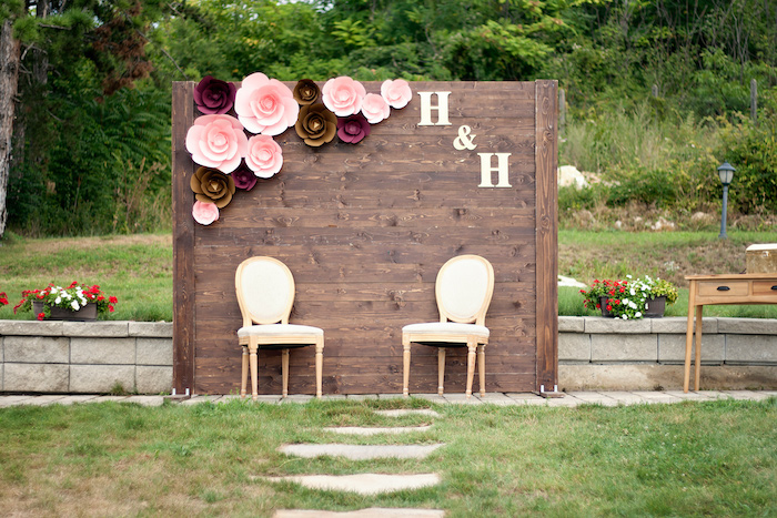 wooden backdrop with pink and brown flowers and initials, trees in the background, rustic wedding ideas