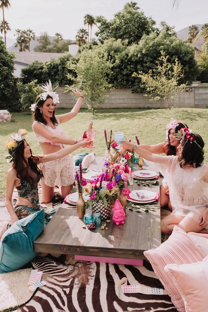 women smiling, women sitting in a garden, flower arrangements on the table, bachelorette party ideas, flower crowns