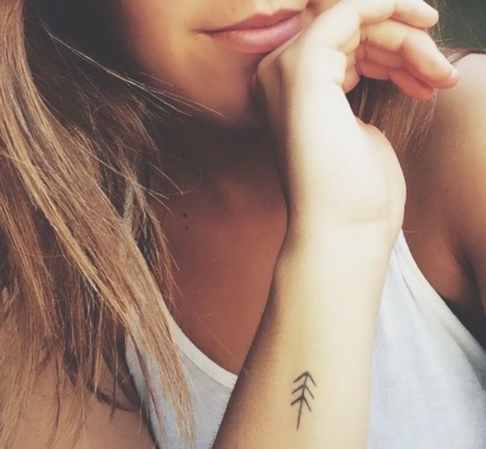 arrow forearm tattoo, small tattoo ideas, woman wearing a white top, with long blonde hair