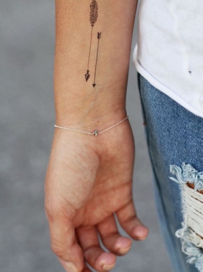 arrows pointing down wrist tattoo, small tattoos for men, woman wearing ripped jeans, white blouse