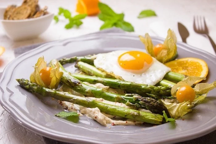 white plate, asparagus and an egg, with cherry tomatoes, lemon slices, balanced diet
