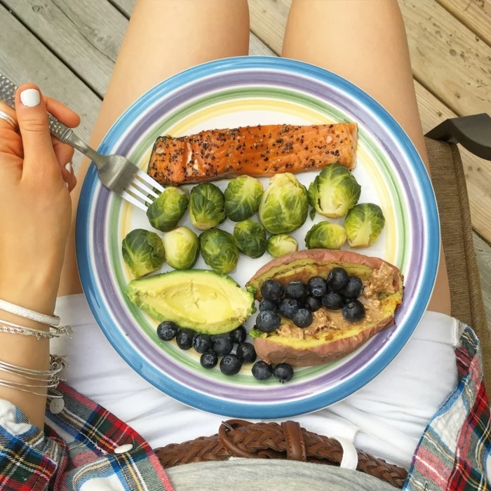 woman holding a plate, full of fish fillet, avocado and blackberries, balanced diet, white jean shorts