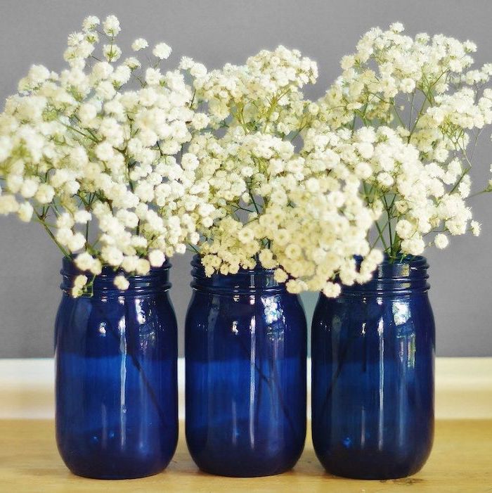 three mason jars, painted in blue, filled with white flowers, kitchen table centerpieces, wooden table
