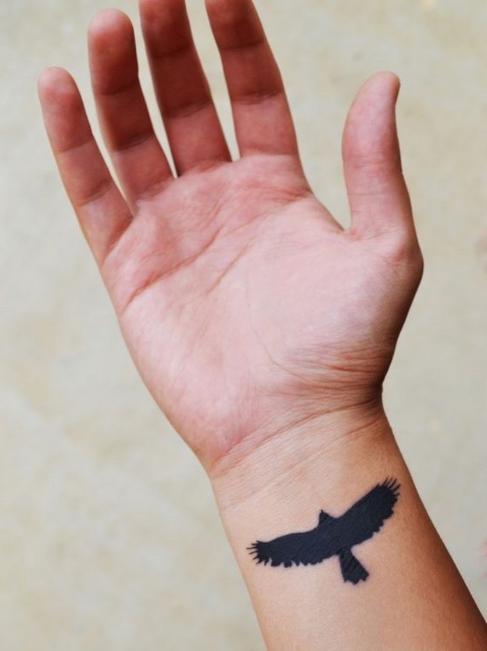 flying black eagle wrist tattoo, small tattoos for men, hand in front of a white background