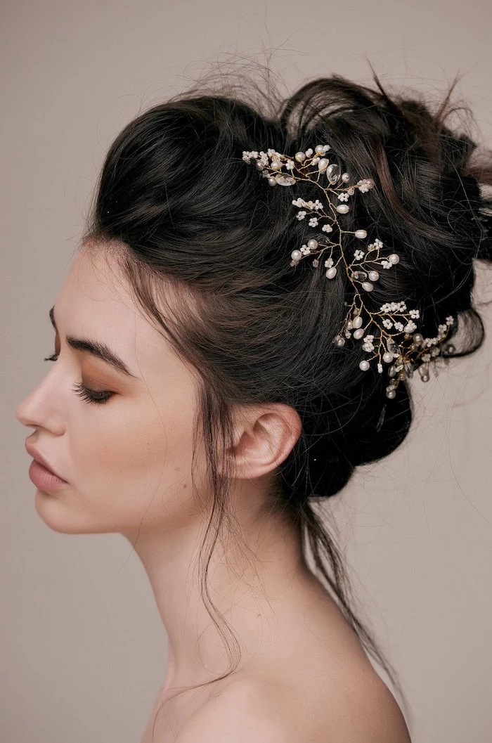 wedding hairstyles for long hair, black hair, in a messy bun, pearl hair accessory, grey background
