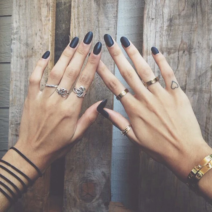 black almond shaped nails, many silver rings, small heart tattoo, finger tattoo ideas, wooden background