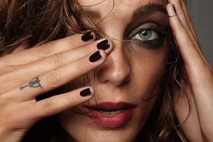 woman with flaking make up, small tattoo on her ring finger, finger tattoo, dark nail polish, green eyes