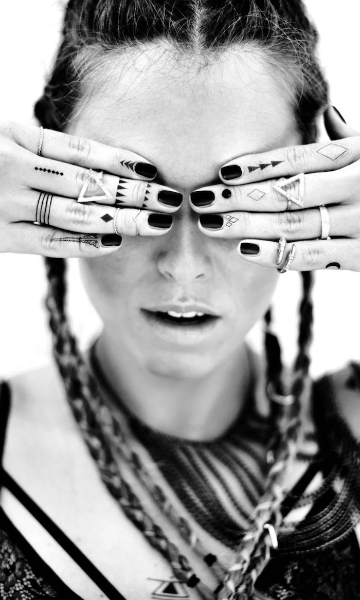 woman covering her eyes, many tattoos on her fingers, finger tattoos, black nail polish, braided hair
