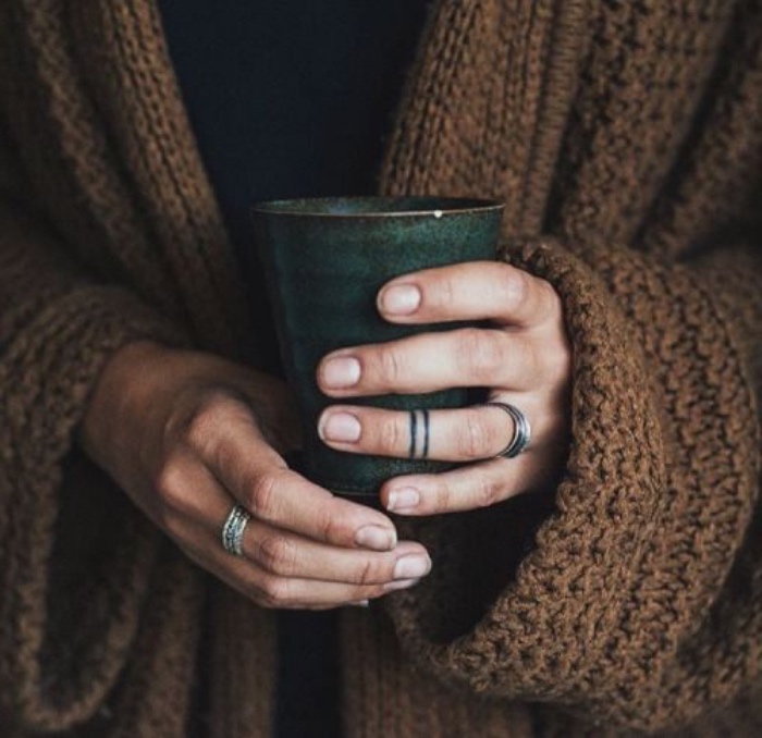 black rings tattoo around the finger. small tattoo, woman wearing a brown cardigan, holding a mug