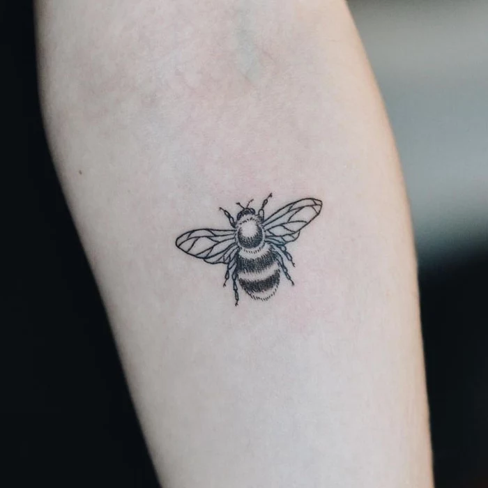 small black and white bee, forearm tattoo, geometric tattoo sleeve, blurred background