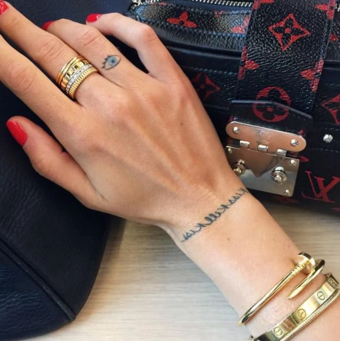 red nail polish, blue eye tattoo, on her ring finger, finger tattoos, golden rings and bracelets