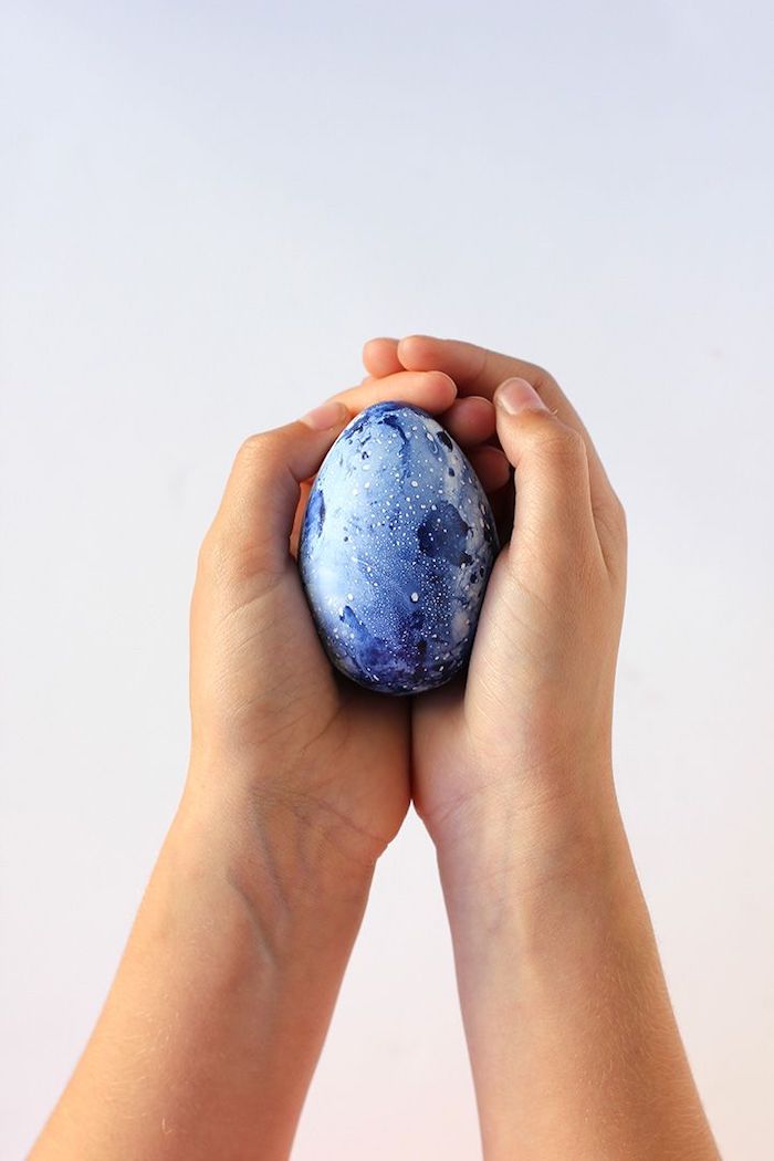blue marble eggs, diy tutorial, easter egg designs, hands holding an egg, in front of a white background