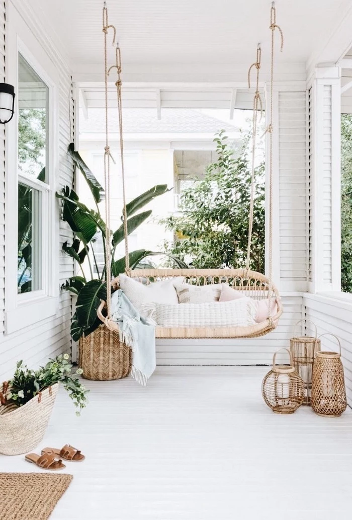 backyard garden ideas, boho style patio, swing with throw pillows, small lanterns, on a white wooden floor
