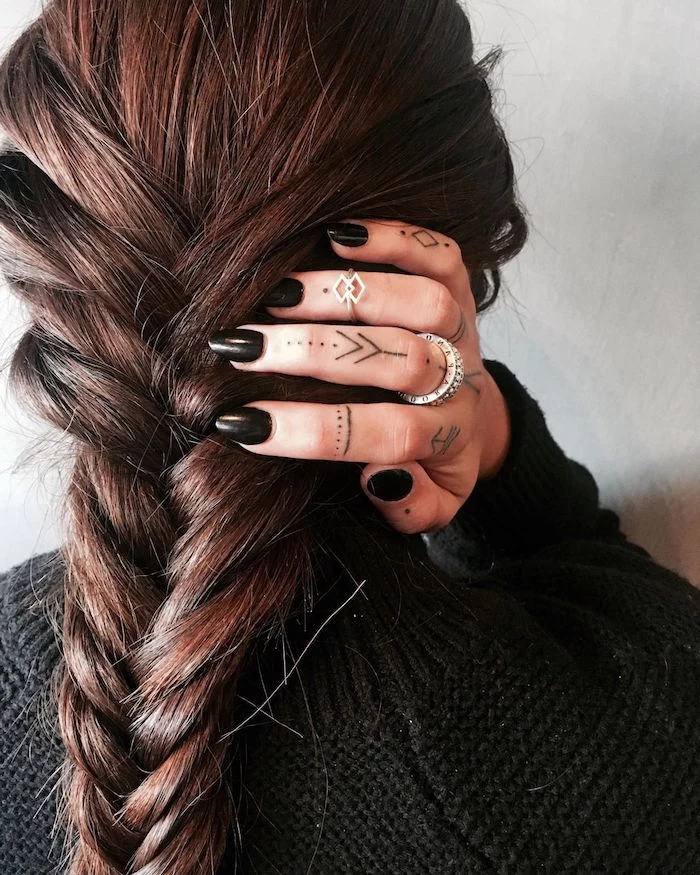 long brown braided hair, hand with many finger tattoos, ring finger tattoos, black nail polish