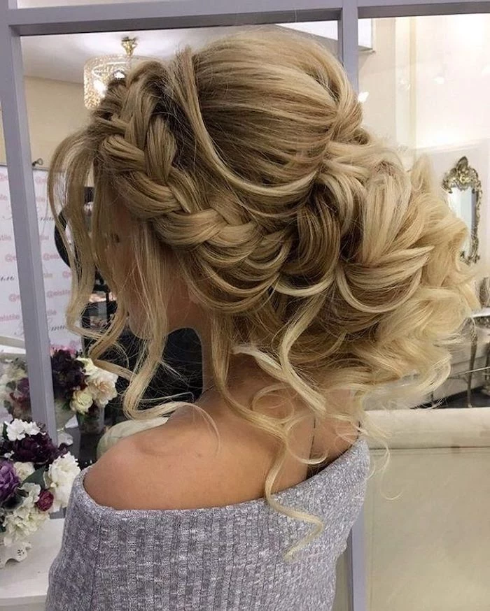 long blonde hair, in a braided updo, wedding hairstyles updo, grey sweater, flower bouquets on the table