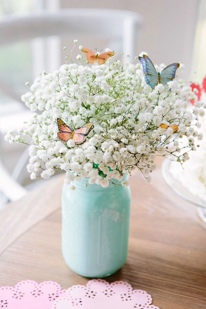 mason jar, painted in light blue, filled with white flowers, small butterfly decorations, floral centerpieces
