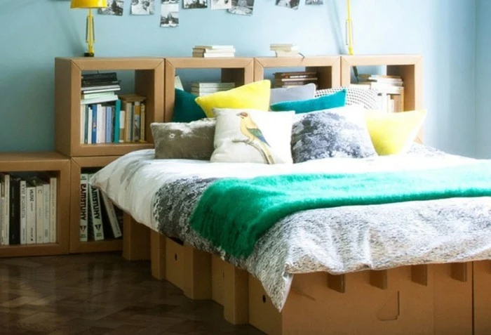 cardboard bed, cardboard shelves, lots of books, green blanket, blue and yellow throw pillows