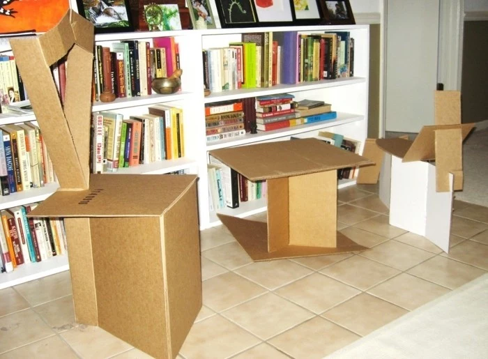 cardboard chairs and table, cardboard shelves, beige tiled floor, large white bookshelf, lots of books