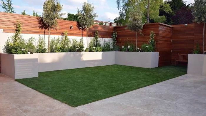 patch of grass, surrounded by cement tiles, planted bushes and trees, garden decoration ideas