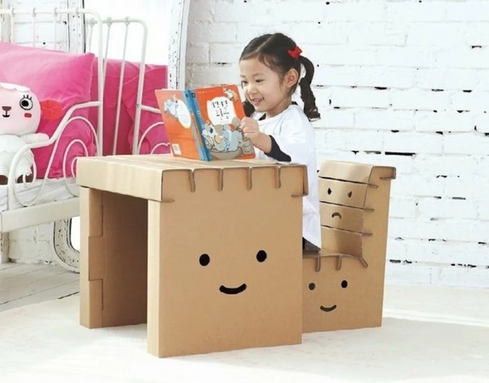 little girl reading, cardboard chair design, children's desk and chair, in front of a white brick wall