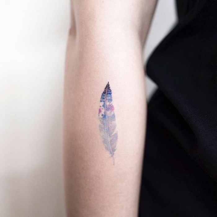 colourful feather forearm tattoo, cool small tattoos, person wearing a black shirt, on a white background
