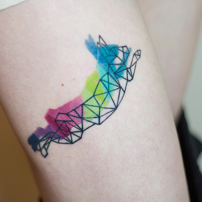 rainbow coloured geometrical rabbit, thigh tattoo, sacred tattoo, blurred background