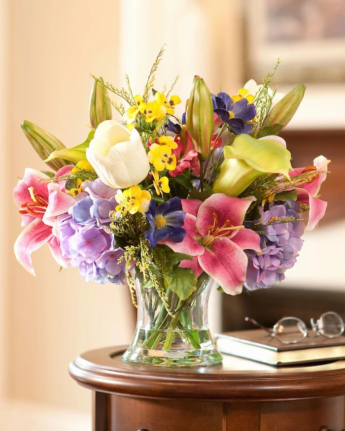 colourful flower, small flower bouquet, on a small wooden table, floral centerpieces, next to glasses and a book