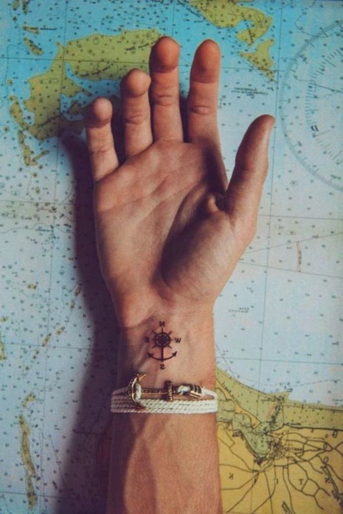 small compass, wrist tattoo, tattoos for men with meaning, hand on top of a map, white anchor bracelet