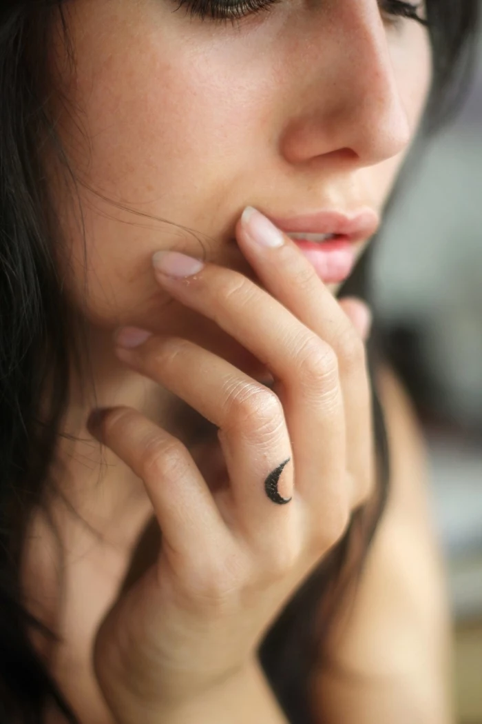 woman holding her hand, next to her face, small crescent moon, ring finger tattoo, finger tattoos for men
