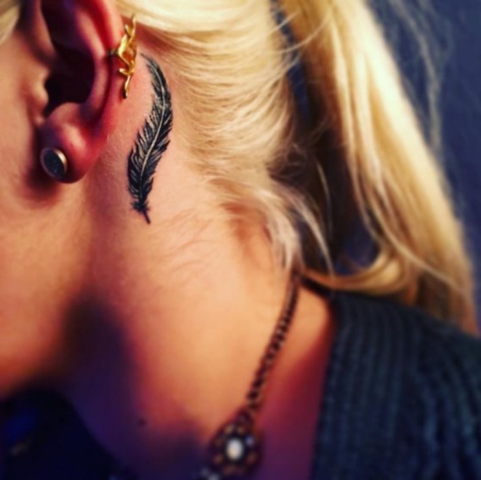 black feather behind the year tattoo, woman with a blonde hair in a ponytail, small meaningful tattoos