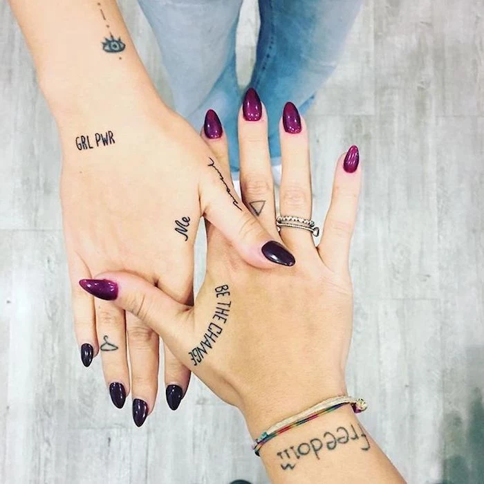two girls, with many tattoos, purple and black nail polish, fingers crossed tattoo, silver rings