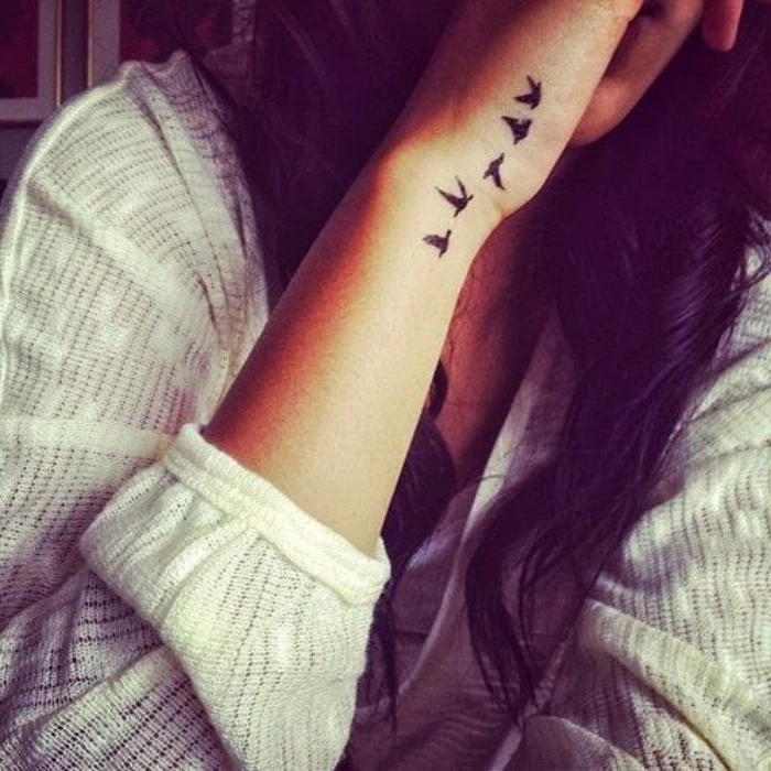 five birds flying away wrist tattoo, small meaningful tattoos, woman with long black hair, wearing a white blouse