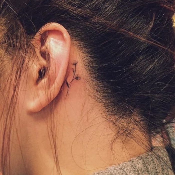 small flower behind the ear tattoo, woman with brown hair in a messy bun, small meaningful tattoos