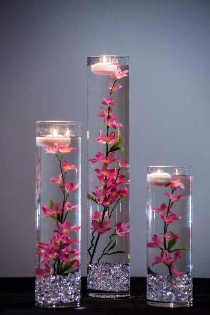 three tall round vases, flowers and candles, floating in the water, silk floral arrangements