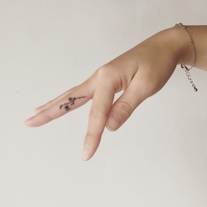 small flower, middle finger tattoo, fingers crossed tattoo, hand in front of a white background, with a silver bracelet