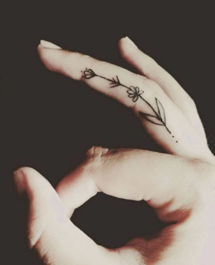 small flower tattoos, middle finger tattoo, fingers crossed tattoo, hand in front of a black background