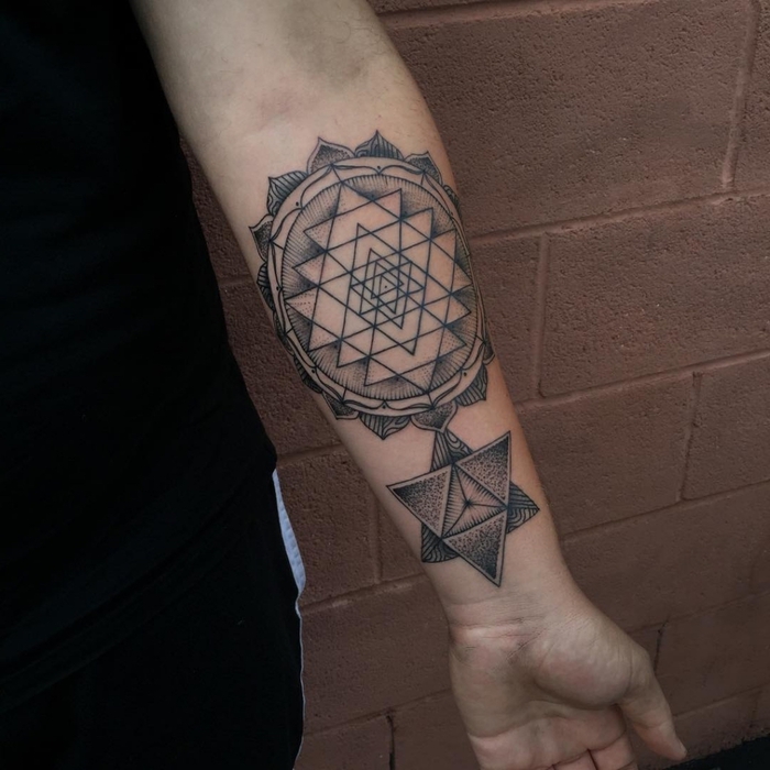 geometrical triangles and circles, forearm tattoo, balance tattoo, brick wall in the background