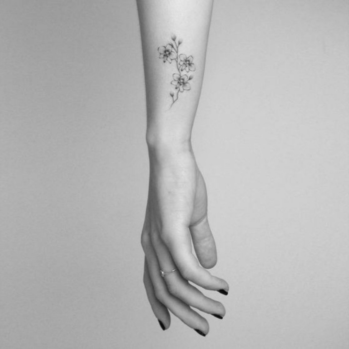 flowers wrist tattoo, woman's hand with black nail polish, in front of a white background, small tattoos with meaning