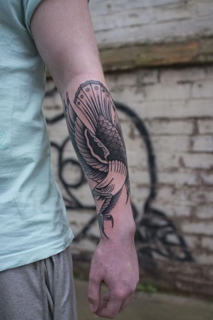 flying eagle, forearm tattoo, shoulder tattoos for men, man wearing a turquoise shirt, grey pants