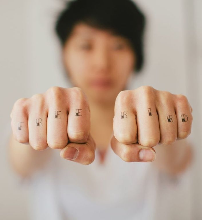 free bird tattoo, one letter on each finger, small finger tattoos, woman in the blurred background