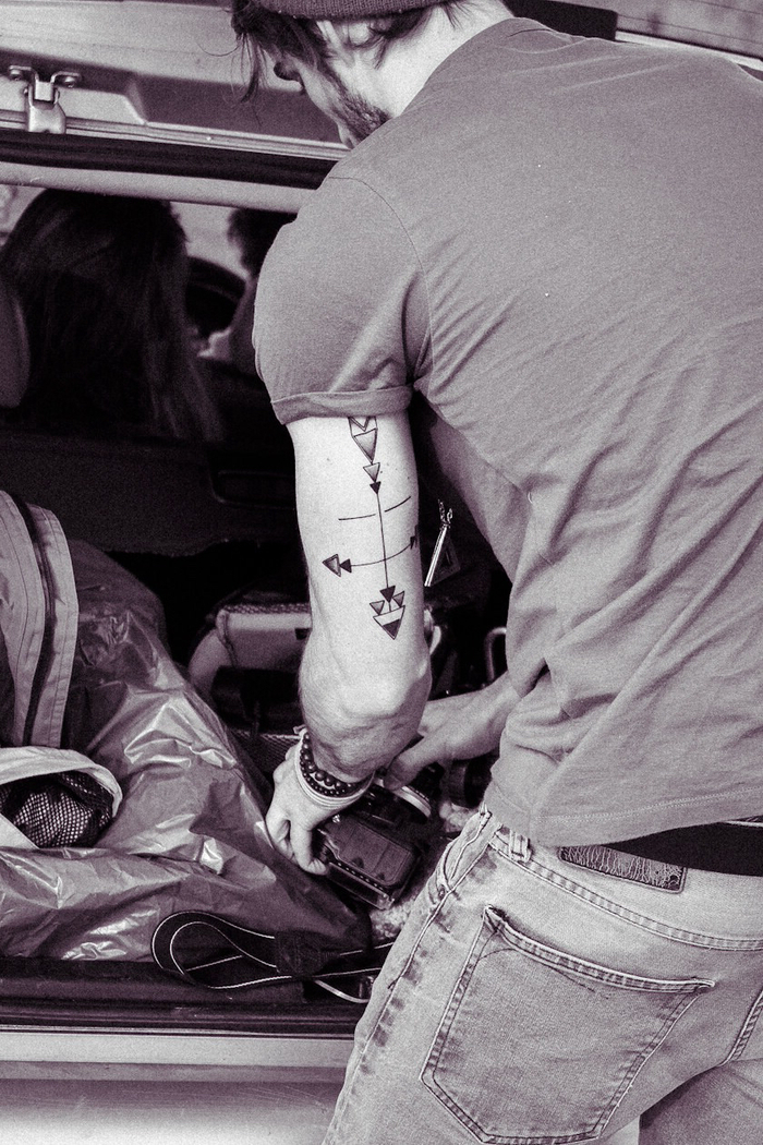 horizontal and vertical arrows, back forearm tattoo, man standing next to a car, putting luggage in the trunk