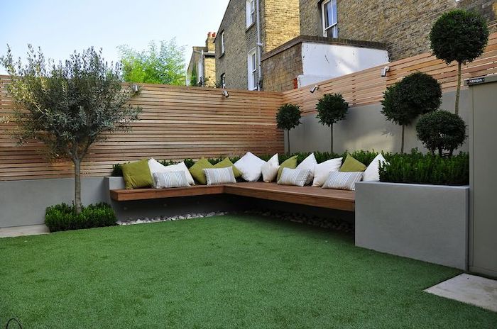 patch of grass, wooden bench, with white and green throw pillows, garden design ideas, planted trees and bushes