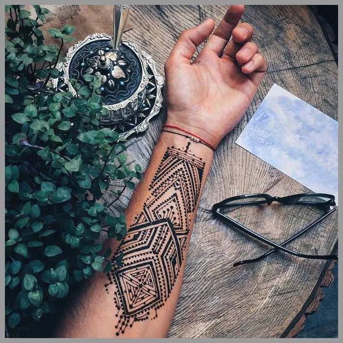 henna design, forearm tattoo, tattoo ideas for men, hand lying on a wooden table, next to glasses and potted plant