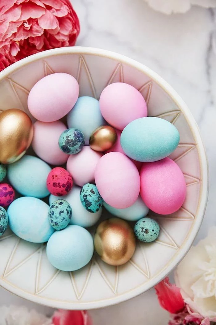 white bowl, full of colourful eggs, blue pink and gold, easter egg coloring ideas, flowers on the side
