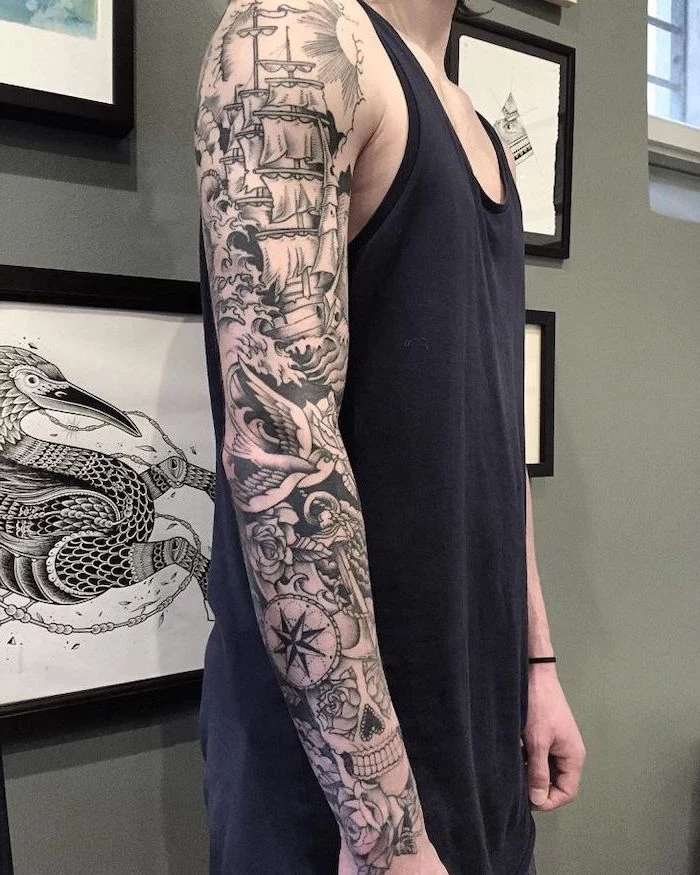 sailing inspired, arm sleeve tattoo, tattoo designs for men, man wearing a black top, standing in front of framed pictures
