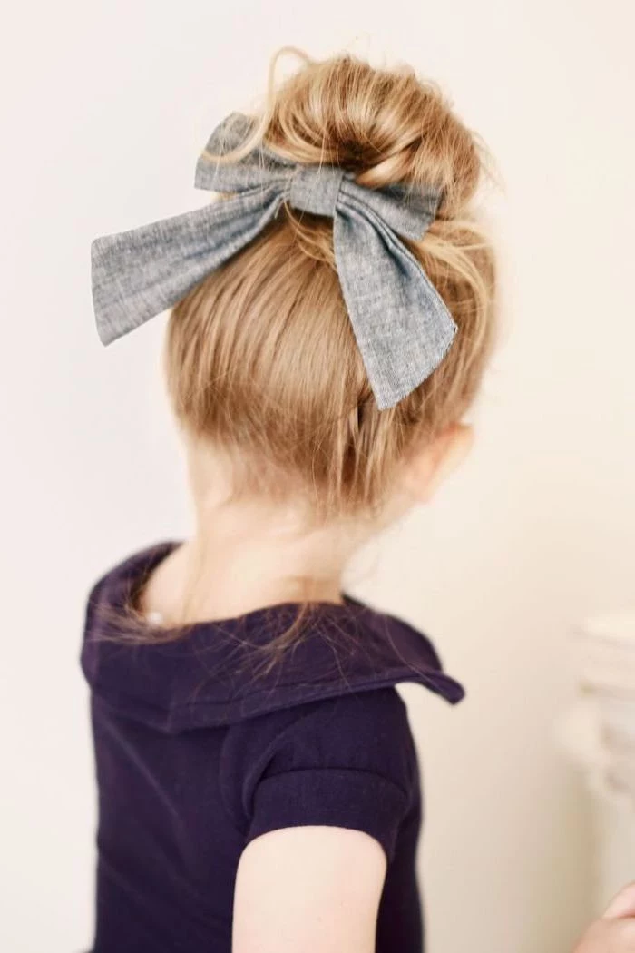 large grey bow, cute hairstyles for little girls, blonde hair in a messy bun, white background, purple top