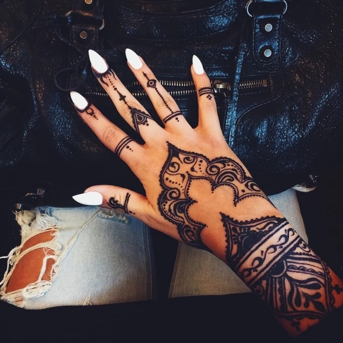 large henna tattoo, white stiletto nails, small finger tattoos, hand resting on a black leather bag